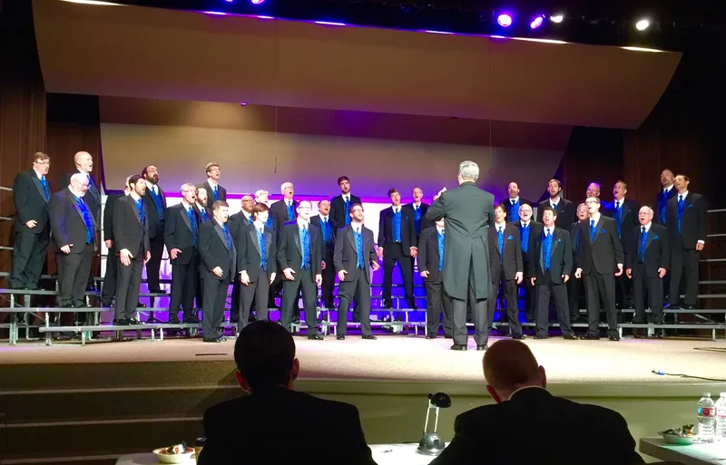 Ted Chamberlain directing a men's chorus on stage during a performance